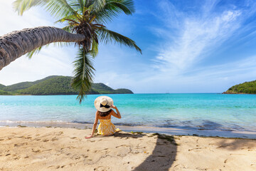A beautiful holiday woman relaxes on a tropical beach under a coconut palm tree in the Caribbean Sea, Antigua and Barbuda island - obrazy, fototapety, plakaty