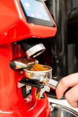 Close-up of a vibrant red coffee machine with freshly ground coffee in a portafilter, ready for brewing. A moment capturing the rich texture of the beans