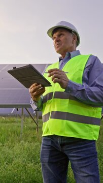 Engineer stands front of solar panels. Holding tablet and checking photovoltaic solar panels.