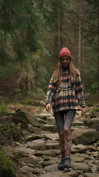 Blonde active woman walking in woods, stepping on rocks, enjoys the nature
