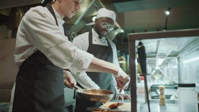 Master chef taking cooked meat steaks from frying pan with tweezers and slicing them while preparing dish in restaurant kitchenMaster chef taking cooked meat steaks from frying pan with tweezers and s