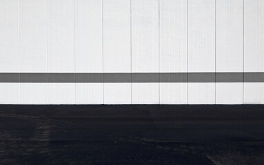 White concrete wall made of vertical blocks with a gray painted horizontal line. Street in front. Background for copy space.