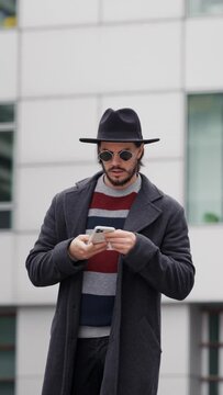 Stylish bearded hipster guy dressed in coat walking on street while calling smartphone device