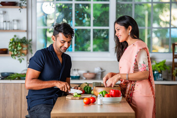 Indian asian young couple chopping or cutting fresh vegetable in home kitchen