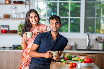 Indian asian pretty young couple having coffee or tea in the mug in kitchen