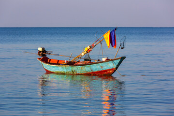 A single small fishing boat rest on the calm sea in the morning light in the eastern Gulf of Thailand.