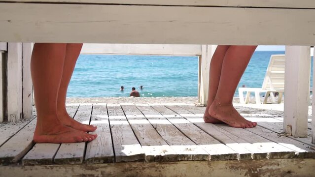 Two woman in the changing, dressing room on beach, at sunset on the seashore. Close-up of bare female feet legs in enclosed changing room cabin. Summer holiday vacation and travel concept. Slow motion