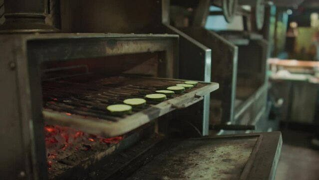 Close up view of hands of unrecognizable chef putting slices of eggplant on grill, then closing charcoal oven while preparing food in restaurant kitchenClose up view of hands of unrecognizable chef pu
