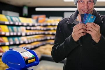 Portrait of happy smiling man holding credit cards near modern self-service terminal in grocery store. Supermarket offers payment card terminals from multiple banks for diverse needs