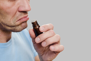 Closeup of man sniffing odor of essential oil bottle suffering from anosmia. Emotional aroma: Man...