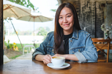 Portrait image of a beautiful young asian woman holding and drinking hot coffee in cafe - 792602226