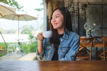 Portrait image of a beautiful young asian woman holding and drinking hot coffee in cafe - 792602256