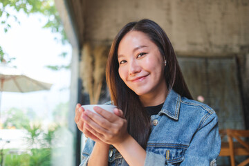 Portrait image of a beautiful young asian woman holding a cup of coffee in cafe