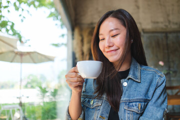 Portrait image of a beautiful young asian woman holding and drinking hot coffee in cafe - 792602406