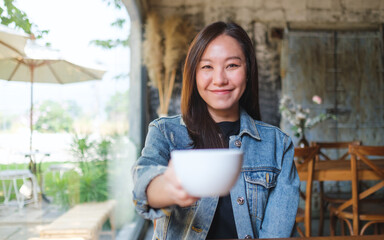 Portrait image of a beautiful woman holding and serving a cup of hot coffee in cafe