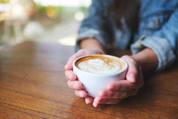 Closeup image of a woman holding a cup of hot coffee with latte art - 792602602