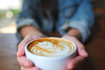 Closeup image of a woman holding a cup of hot coffee with latte art - 792602607