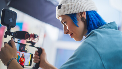 Young Caucasian Female Cinematographer With Blue Hair Adjusts Camera Settings On Film Set,...