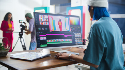 Young Caucasian Female Editor With Blue Hair Works On Video Editing Software, While A Hispanic Male Videographer Records A Black Female Host In A Vibrant Studio Setting, Enhancing Media Production.