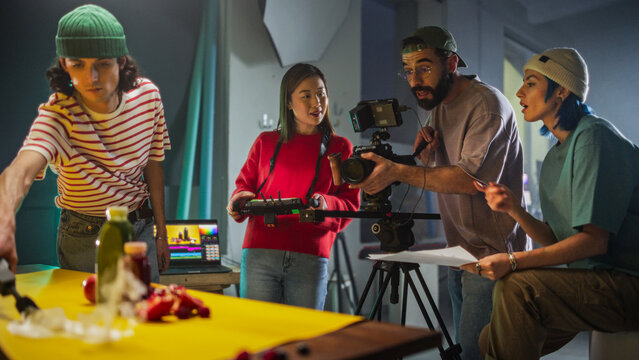 Dynamic Young Film Crew Engaged In A Lively Discussion On A Colorful Set, With A Female Asian Cinematographer Adjusting A Camera As Her Diverse Team Collaborates On A Creative Video Production Project - Powered by Adobe