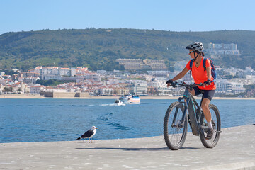 nice senior woman cycling with her electric mountain bike on the fishermens jetty of Sesimbra, Portugal - 792603828
