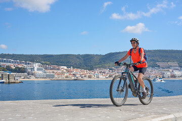 nice senior woman cycling with her electric mountain bike on the fishermens jetty of Sesimbra, Portugal - 792603891