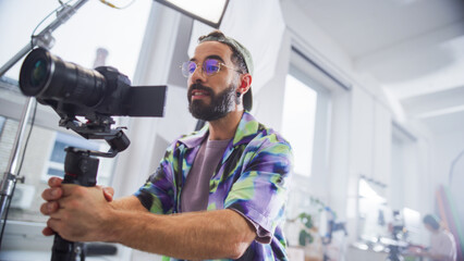 Focused Male Cinematographer With Beard, Wearing Colorful Shirt, Operates Professional Camera In...