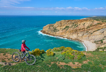 nice active woman cycling with her electric mountain bike on the cliffs of Cabo Espichel near Sesimbra, Portugal