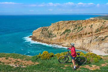 nice active woman cycling with her electric mountain bike on the cliffs of Cabo Espichel near Sesimbra, Portugal - 792606889