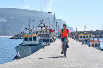 nice senior woman cycling with her electric mountain bike on the fishermens jetty of Sesimbra, Portugal - 792609467