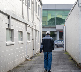 Man walking between building walls towards the car parked on the street.