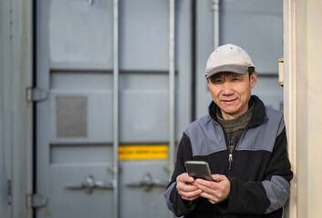 Worker taking a break and checking his smartphone. Standing between containers on a construction site.  - 792616891