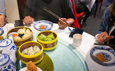 Hands holding chopsticks. Yumcha, dim sum in bamboo steamers. Chinese cuisine. - 792618204