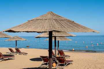 Sandy beach in Fujairah, United Arab Emirates, with thatch umbrellas and sunbeds, sea view and blue...