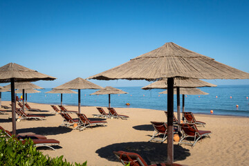 Sandy beach in Fujairah, United Arab Emirates, with thatch umbrellas and sunbeds, sea view and blue sky, no people.