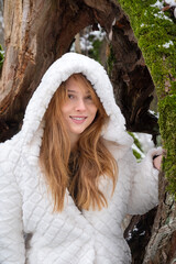 Portrait of a beautiful sexy seductive young happy smiling woman outside holiday in nature tree forest in the cold snowy winter with white coat