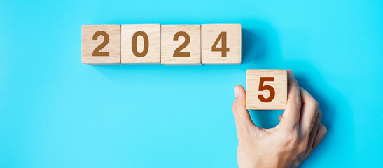 hand holding wooden cube block with 2025 text on blue background. Resolution, plan, review, goal,...