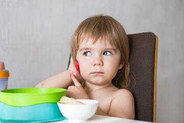 Adorable toddler girl sitting at table with food and drink and playing with spoon. - 792623865