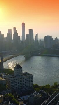 Manhattan and Brooklyn Bridges over East River at Golden hour. Hazy silhouettes of striking skyscrapers at backdrop of orange sky. Vertical video