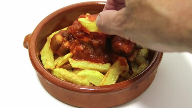 Dogfish in tomato sauce with French fries. Served in a clay bowl. Isolated on a white background. A hand picking up a potato. Spanish food concept.