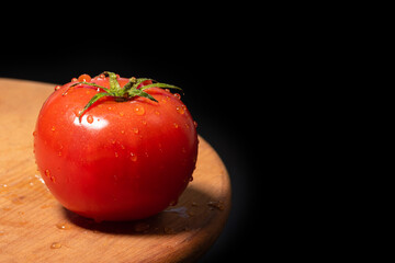 Ripe tomato on a wooden board isolated against black background. - 792633223