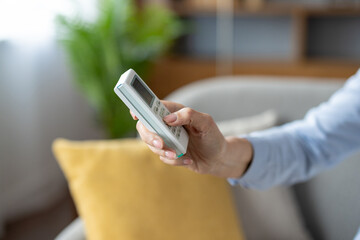 A close-up view of a female hand using a remote control to adjust settings in a cozy, modern living room setting.