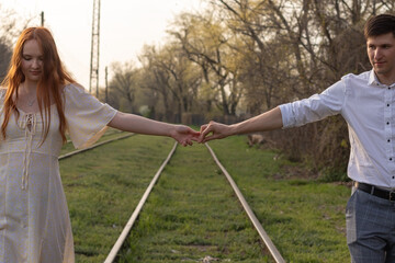 Young  man and woman holding hands and walking along railway tracks toward camera at sunset.
