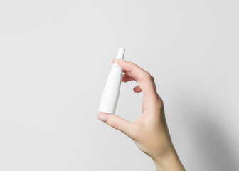 hand holding a white bottle with nasal spray on white background