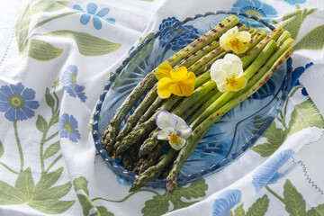 Bunch of green asparagus. Fresh spring vegetable on blue plate. Pansy flowers. Asparagus grill...