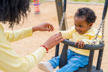Little african girl swinging with her mother in a park
