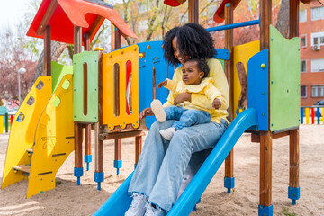 African mother with baby on lap sliding in playground