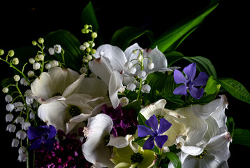 Close up bouquet of beautiful spring flowers on a black background. Dogwood flowers, lilies of the valley, lilac, periwinkle, green leaves. low key photo.