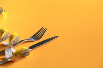 Measuring tape around fork and knife on yellow background. Weight loss and healthy concept