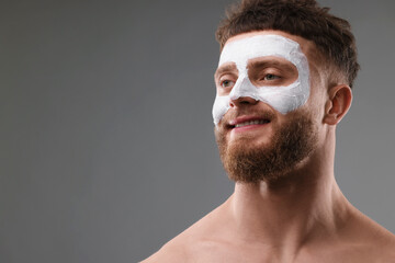 Handsome man with facial mask on his face against grey background, space for text